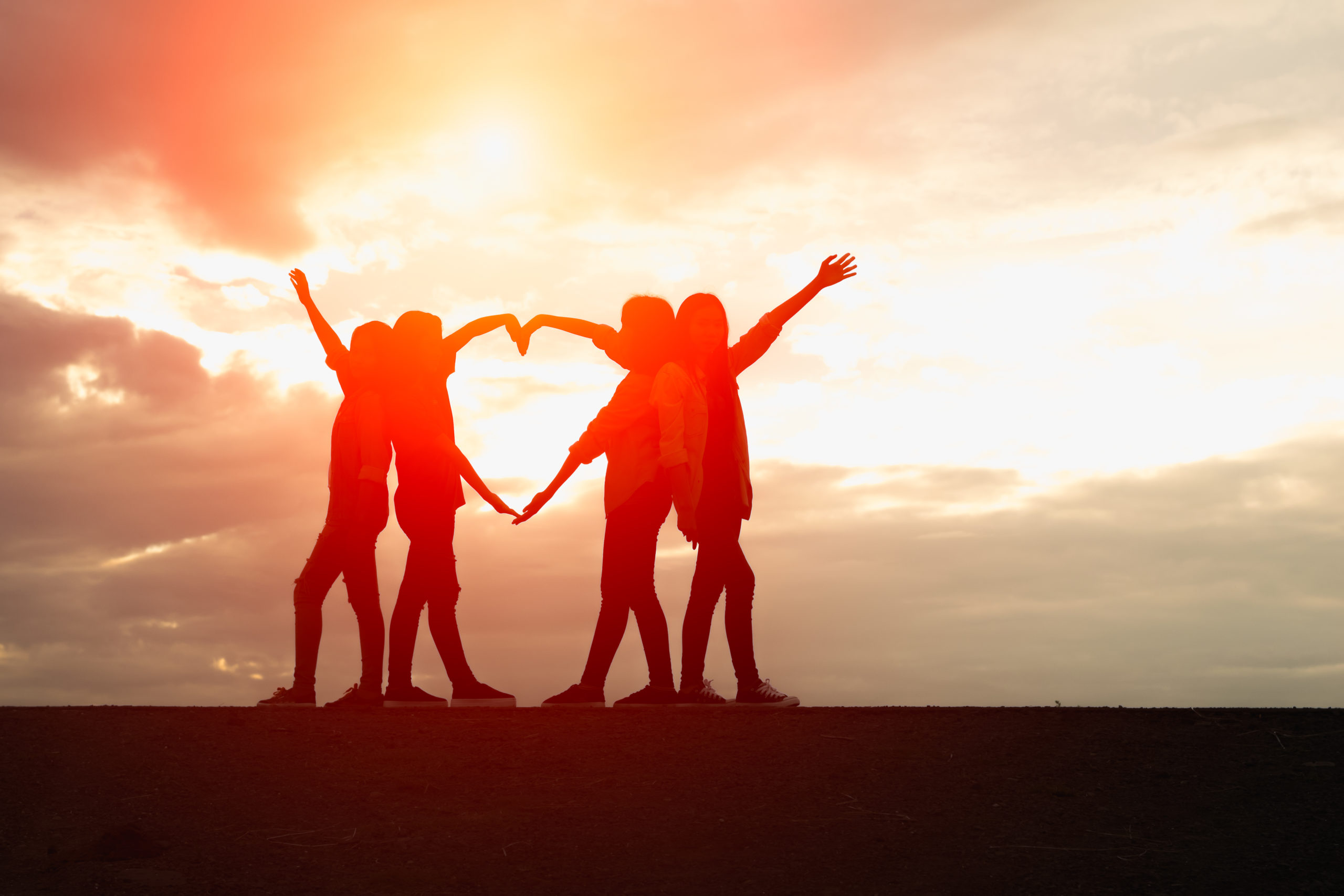 Four female silhouettes hands making a heart shape with sunset b